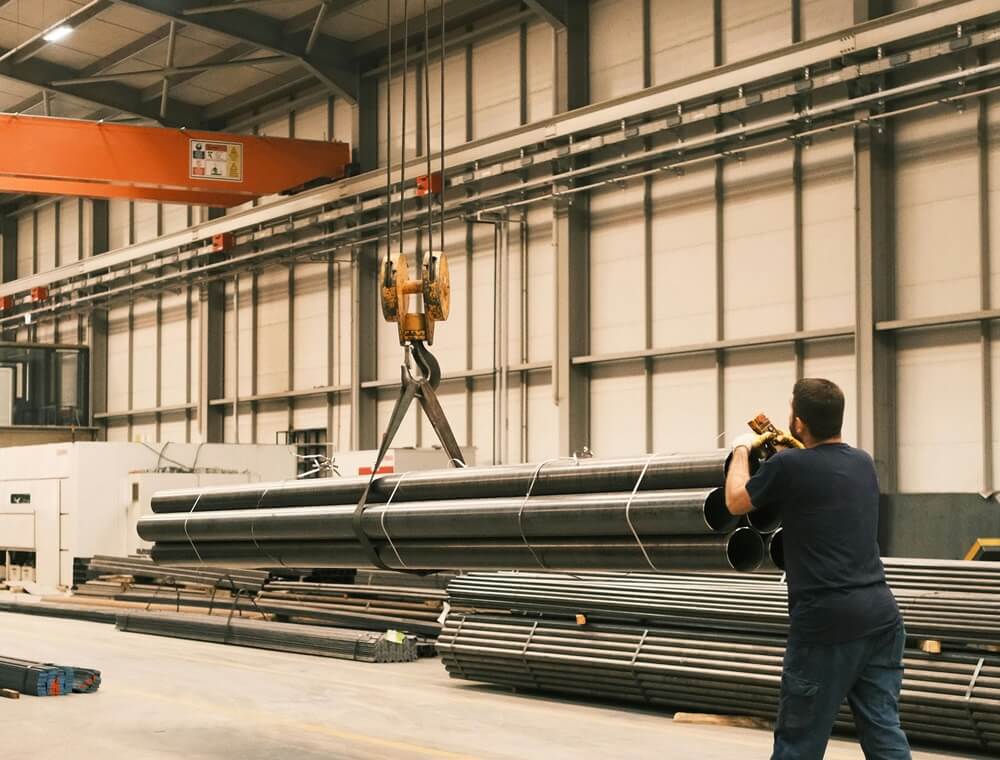 Warehouse worker using hoist to carry metal pipes